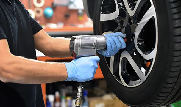 Mechanic wearing blue gloves using an impact wrench to tighten a car wheel lug nut.