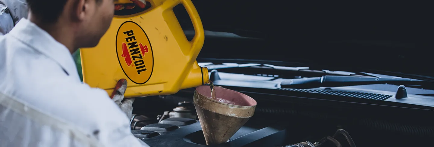 Mechanic pouring Pennzoil motor oil from a yellow container into a funnel placed in a car engine.