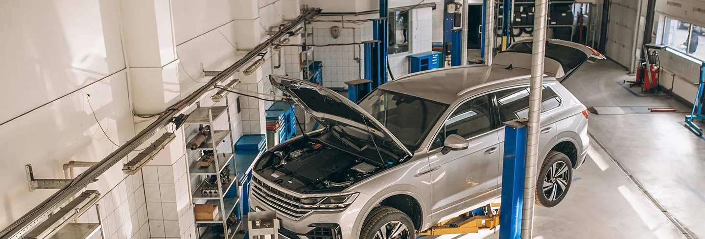 Silver SUV with open hood and trunk elevated on a hoist inside a clean automotive repair shop.